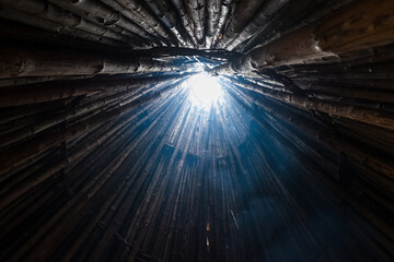 Wooden tipi with smoke going through the whole in roof. Conical light wooden medieval building with fireplace in the middle. View from inside looking up. © Cloudy Design