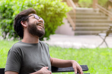 Fototapeta premium Man with beard and glasses laughing sitting on bench in park