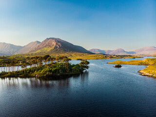 Aerial view of Twelve Pines Island, standing on a gorgeous background formed by the sharp peaks of a mountain range called Twelve Pins or Twelve Bens, Connemara, Ireland