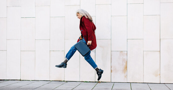 Mature woman with grey long hair jumping on the street. 