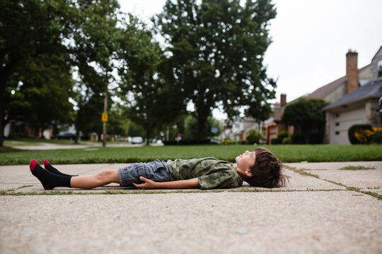 boy lays in driveway and watches clouds 