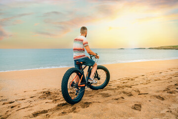 Unrecognizable young man from behind looking at the sea riding a fat bike on the beach