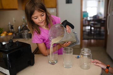 child pours green smoothie into cups