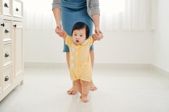 Happy young mother watching her baby taking first steps