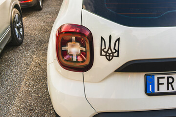 The State Emblem of Ukraine on a white body of a car with an EU license plate on an asphalt road,...