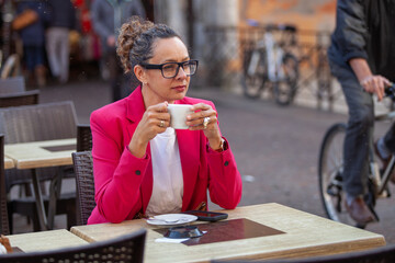 portrait of business woman in pink jacket drinks coffee in street cafe