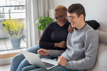 mixed couple with laptop computer at home  on couch, smiling
