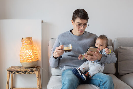 father reading emails on his phone while holding baby son