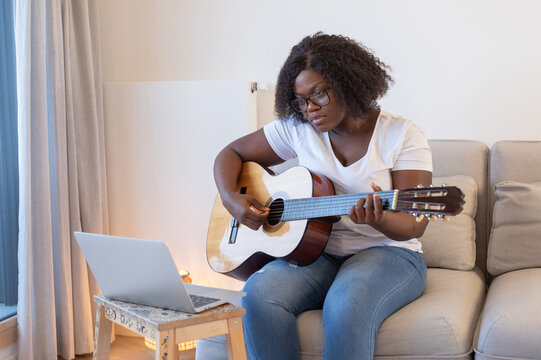 black woman learning to play guitar online at home