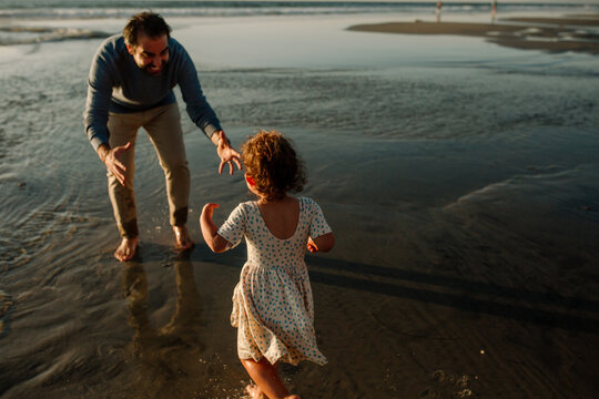 Father reaching for daughter on sea shore