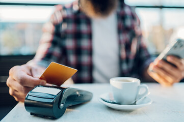 Man making transaction while using credit card and a payment terminal in a cafe