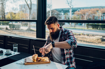 Bearded man sitting in a restaurant and eating a fresh tasty burger