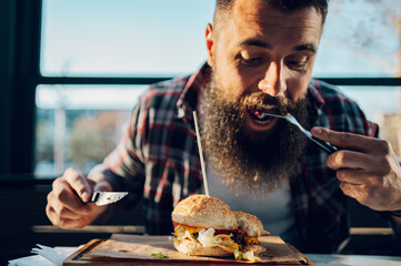 Bearded man sitting in a restaurant and eating a fresh tasty burger