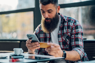 Bearded man using smartphone and a credit card in a cafe or restaurant