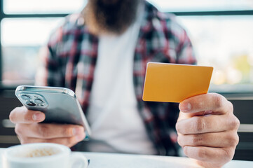 Bearded man using smartphone and a credit card in a cafe or restaurant