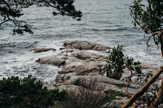 View of rocky and stormy ocean shoreline on a grey day. - Powered by Adobe