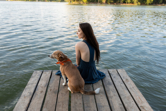 Girl with dog sitting on bridge near river