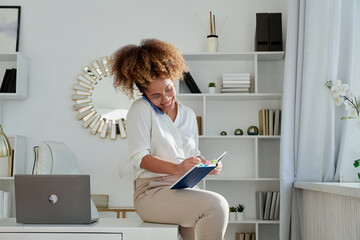 Businesswoman chatting on cell phone sitting at desk 