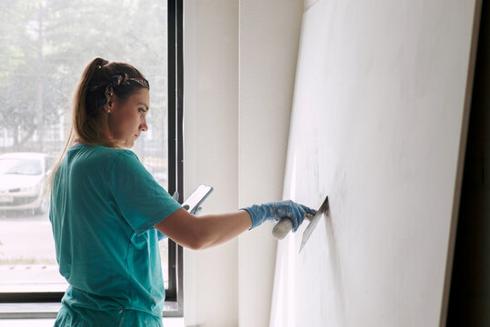 Portrait of woman plasterer with a spatula at work near the wall 