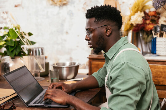 Serious black man using laptop in flower shop