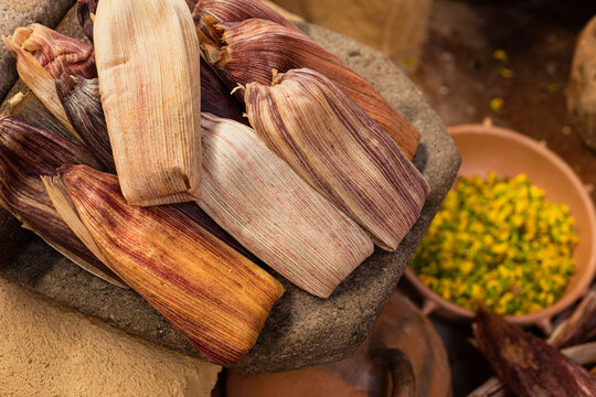 Mexican tamales on a metate and a bowl with flowers next to it 