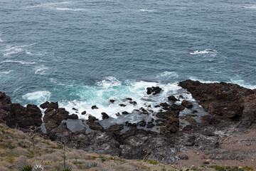 Sea waves hitting rocks in front of a mountain