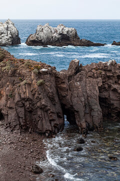  A cliff on a beach with a rock in the blue sea full of guano