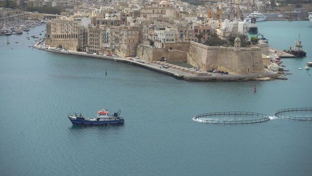 A ship towing fish farming equipment across the Grand Harbour, Valletta