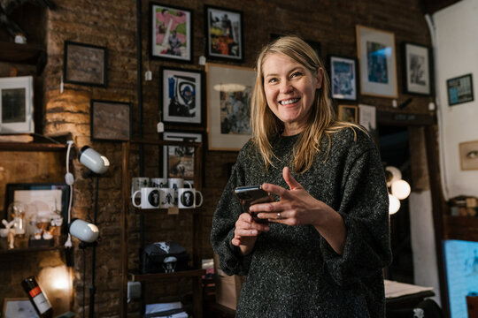 Smiling artist browsing smartphone in art studio