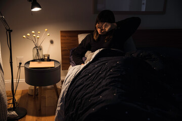 Tired sleepy woman sits in bed rubbing her eyes 