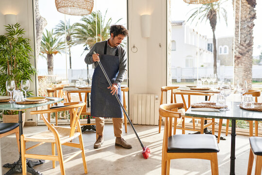 Waiter tidying floor in sunlit restaurant