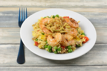 Shrimp with vegetables and white wild rice on white plate with blue fork