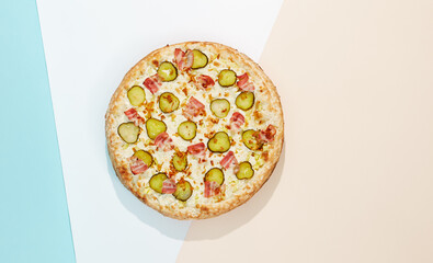 Italian pizza with bacon, pickled cucumber and crispy onion on coloured background. Homemade pizza in minimal style on blue and orange color. American pizza delivery concept with color backdrop.