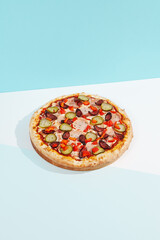 Italian pizza with sausage, jalapeno, ham and paprika on coloured background. Spicy pizza with jalapeno in minimal style on blue and orange color. American pizza delivery concept with color backdrop.