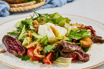 Green salad with sliced roast beef and pachot egg. Roast beef salad with vegetables and egg on concrete background in minimal style. Aesthetic composition with meat salad, textile and spices.