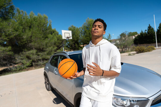 Male athlete with ball leaning on car