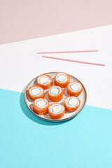 Philadelphia maki roll on ceramic plate with chopsticks. Salmon sushi roll with philadelphia cheese on coloured background. Japanese menu concept. Salmon sushi roll in modern style.