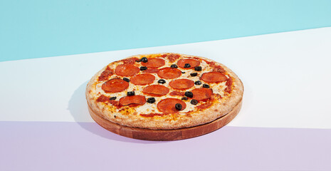 Italian pizza with pepperoni and olives on coloured background. Pepperoni pizza in minimal style on...