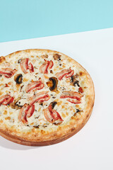 Italian pizza with mushroom and bacon on coloured background. Mushroom pizza with bacon in minimal style on blue and orange color. American pizza delivery concept with color backdrop