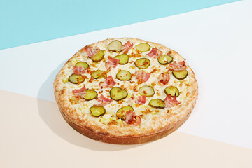 Italian pizza with bacon, pickled cucumber and crispy onion on coloured background. Homemade pizza in minimal style on blue and orange color. American pizza delivery concept with color backdrop.