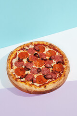 Italian pizza with sausage, salami, pepperoni on coloured background. Meat pizza with salami and pepperoni in minimal style on blue color. American pizza delivery concept with color backdrop.