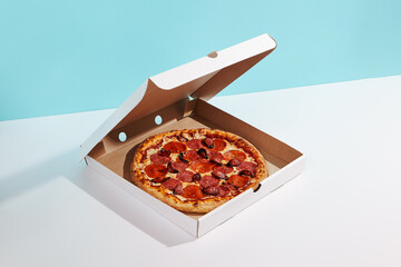 Italian pizza in paper box on coloured background. Meat pizza with sausage and salami in delivery box in minimal style . American pizza delivery concept with color backdrop.