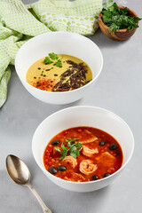 Composition with cream soup and tomato seafood soup. Set of soups on concrete background. Aesthetic composition with vegetables soup and fish soup in white ceramic bowl