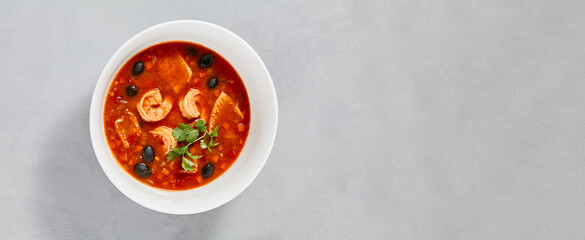 Fish tomato soup with shrimps and black olives. Seafood soup with prawns in white ceramic bowl on concrete background. Fish dish with seafood. Tomato soup in minimal composition.