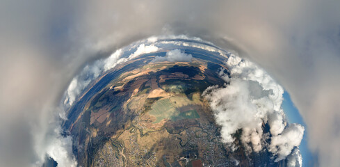 Aerial view from high altitude of little planet with distant city covered with puffy cumulus clouds...
