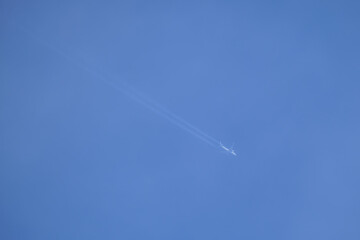 Distant passenger jet plane flying on high altitude on clear blue sky leaving white smoke trace of contrail behind. Air transportation concept