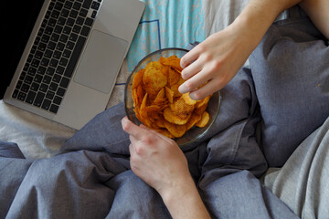 Crop guy eating chips while watching video on laptop