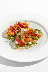 Bruschetta with salmon, avocado and paprika on white plate. Salmon bruschetta on crispy focaccia. Appetizer with guacamole, trout, cheese and paprika on toast. Fish antipasti in restaurant menu.
