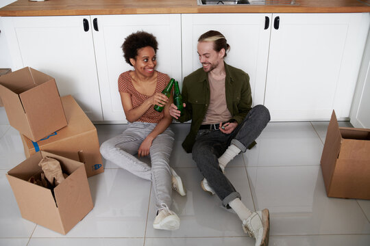 A couple in the new house sits on the floor and drinks beer.