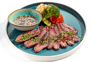 Roast beef with vegetables and sauce on trendy plate. Sliced meat steak roast grill with tomatoes and broccoli isolated on white table. Angus roast beef in healthy style for restaurant.